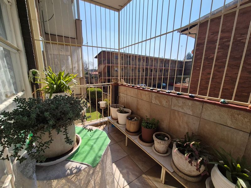 A balcony area featuring tiled flooring, tiled wall cladding, and protective metal security bars, overlooking the surrounding residential complex.