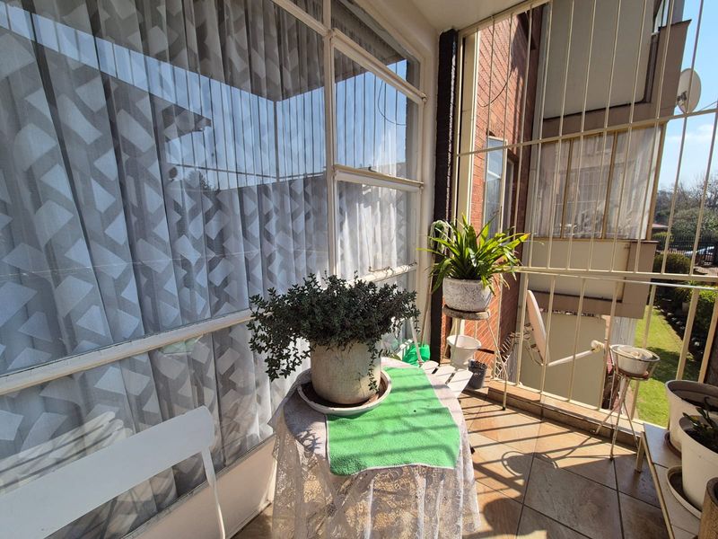 A sunlit enclosed balcony featuring tiled flooring and large windows with security bars, offering a bright space for relaxation.