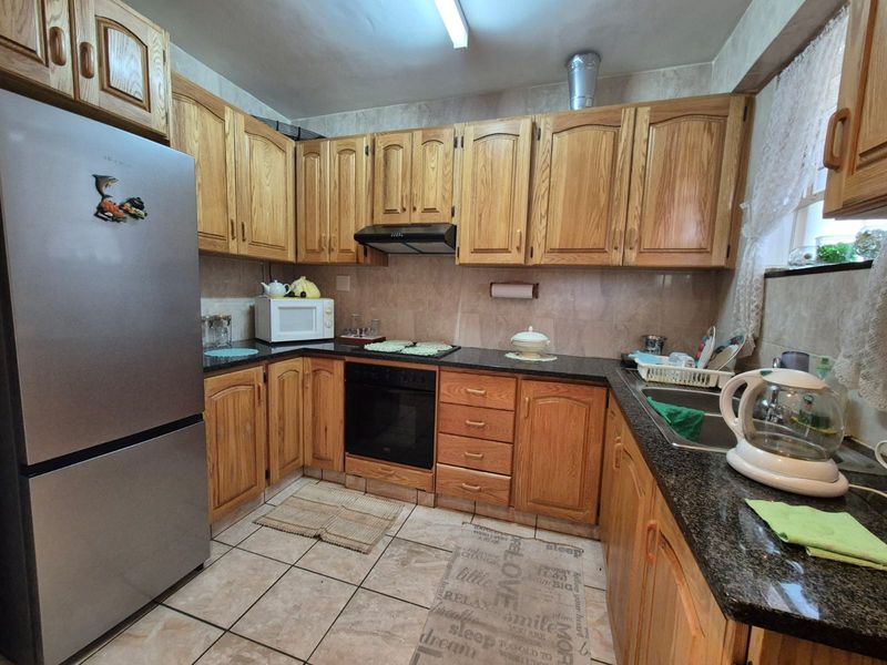 A functional kitchen featuring traditional wooden cabinetry, granite countertops, a built-in oven with extractor fan, and tiled finishes throughout.