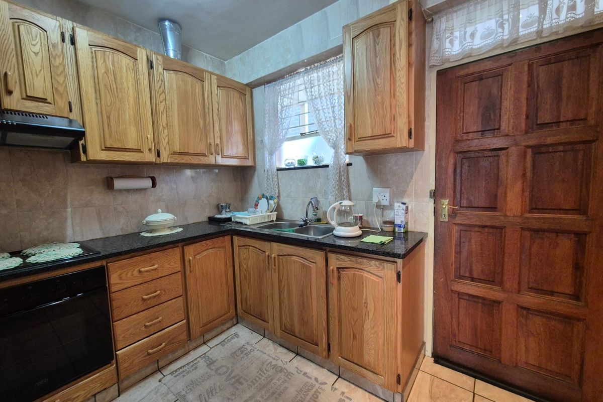 A functional kitchen featuring traditional wooden cabinetry, granite countertops, built-in oven, extractor fan, and tiled finishes throughout.
