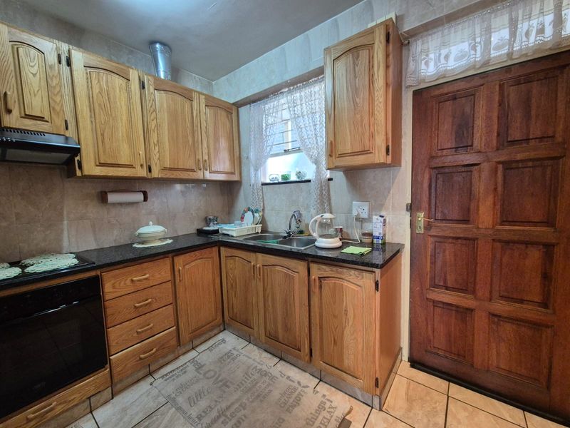 A functional kitchen featuring traditional wooden cabinetry, granite countertops, built-in oven, extractor fan, and tiled finishes throughout.