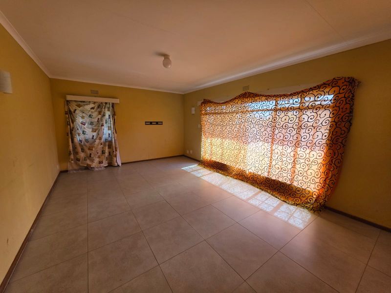 A spacious, empty living room featuring neutral tiled flooring and large windows, providing a blank canvas for potential interior design updates.