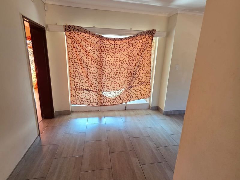 An empty living area featuring neutral tiled flooring, coved ceilings, and a sliding door providing access to the exterior.