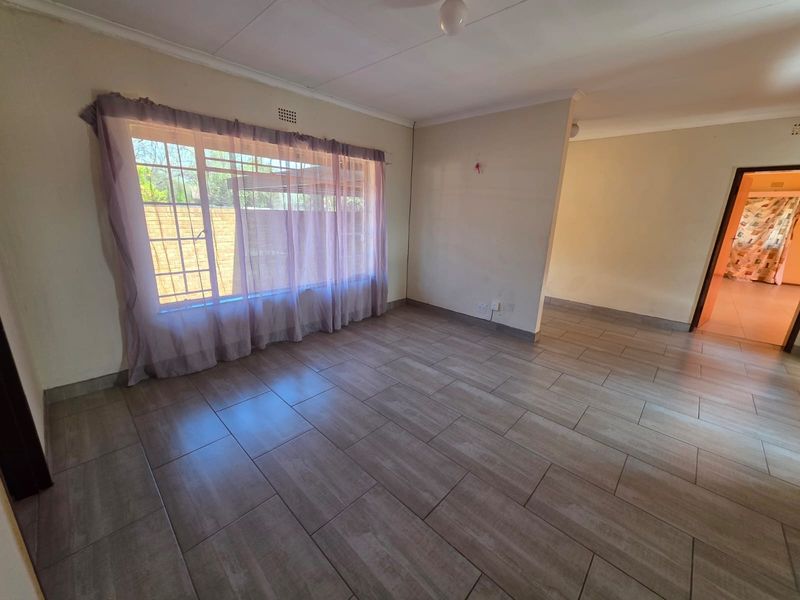 A spacious, empty living area featuring neutral tiled flooring, coved ceilings, and large windows fitted with security bars.