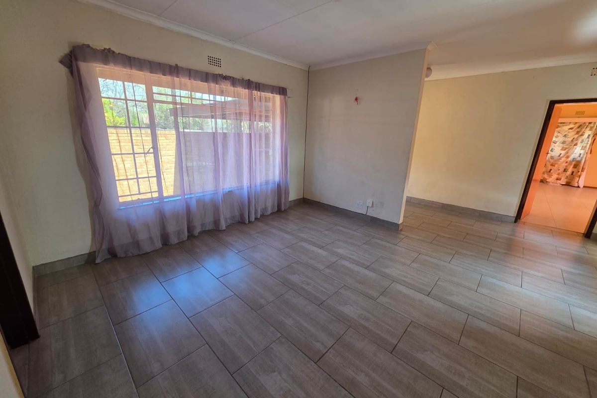 A spacious, empty living area featuring neutral tiled flooring, coved ceilings, and large windows fitted with security bars.