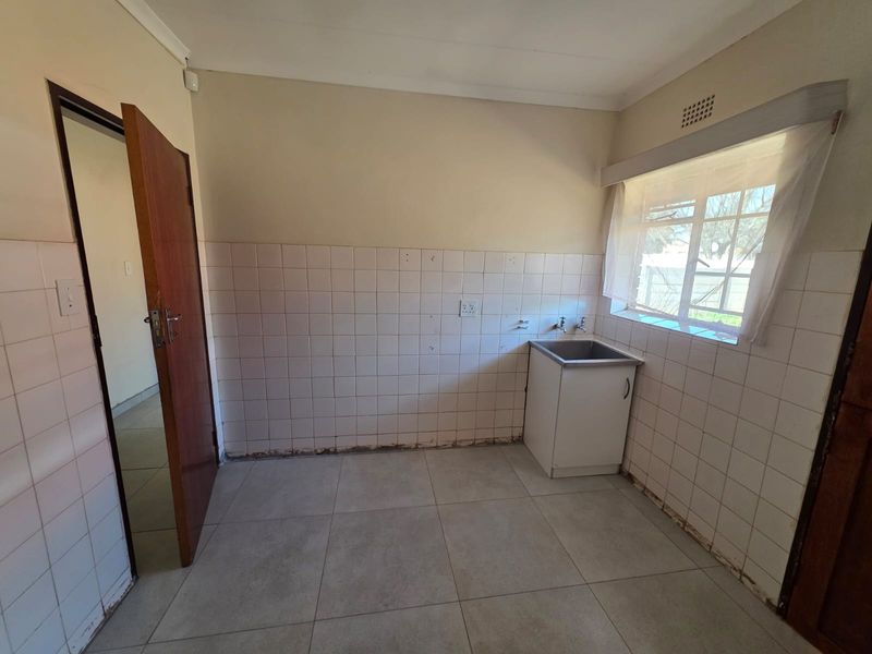 A functional laundry room featuring tiled flooring, a stainless steel sink with cabinet, and tiled splashbacks, ready for modernization.