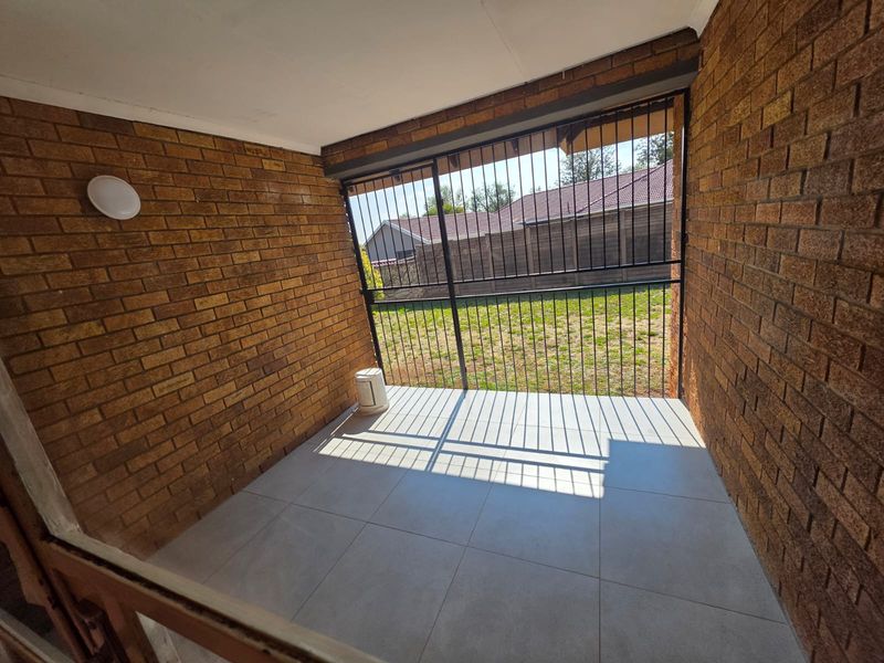 A covered patio area featuring exposed brick walls, modern tiled flooring, and a secure metal gate overlooking the rear garden.