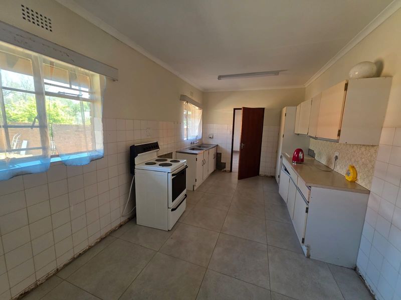 A functional kitchen featuring tiled flooring, a freestanding stove, double sink, and ample built-in cabinetry with a tiled splashback.