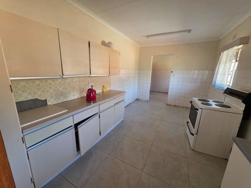 A dated kitchen featuring tiled flooring, tiled splashbacks, and original cabinetry, offering significant potential for a modern renovation and layout update.