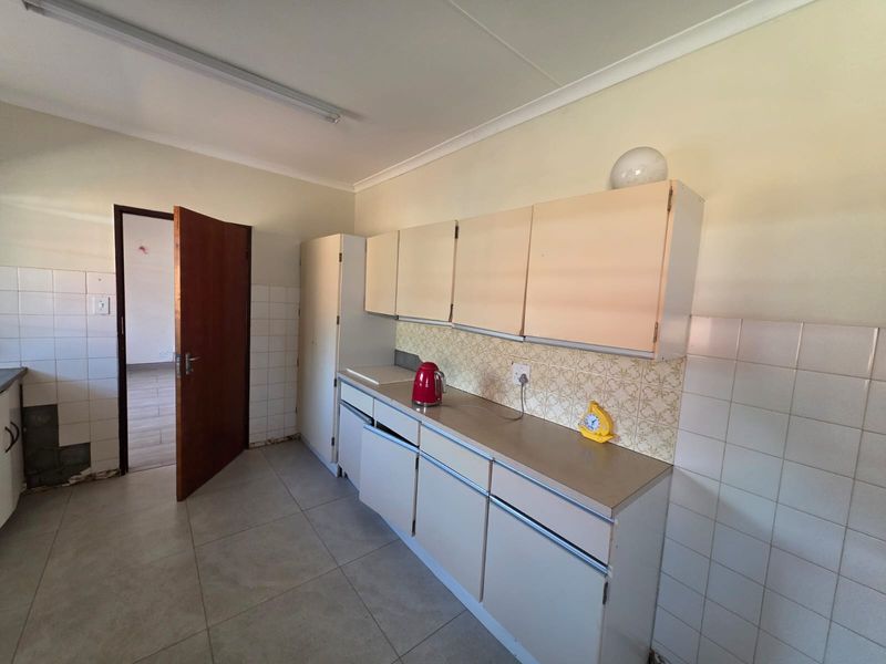 A dated kitchen featuring built-in cabinetry, tiled splashbacks, and tiled flooring, currently requiring cosmetic updates and repairs to the cabinetry and wall finishes.