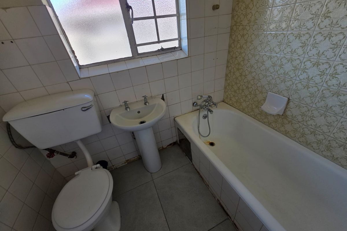 A dated bathroom featuring a pedestal basin, bathtub, and toilet with original wall tiling, requiring renovation to modernize the space.