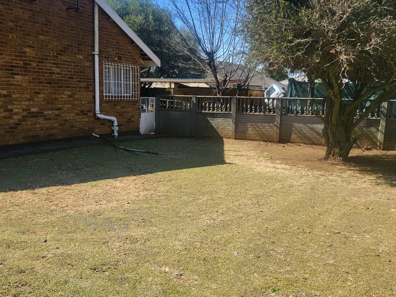 A view of the rear garden featuring a brick exterior wall, security window bars, and a perimeter precast concrete boundary wall.