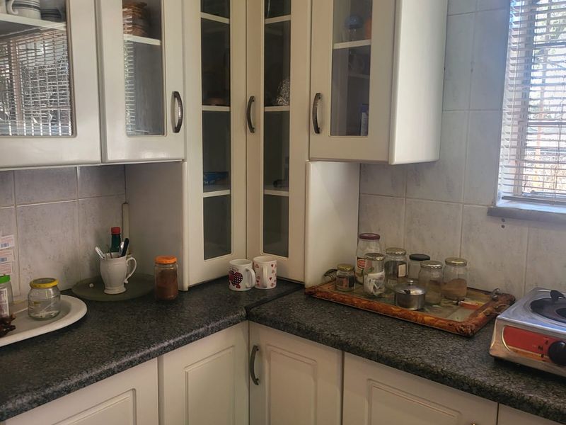 A functional kitchen corner featuring white built-in cabinetry with glass-fronted upper units, dark granite countertops, and a tiled backsplash.
