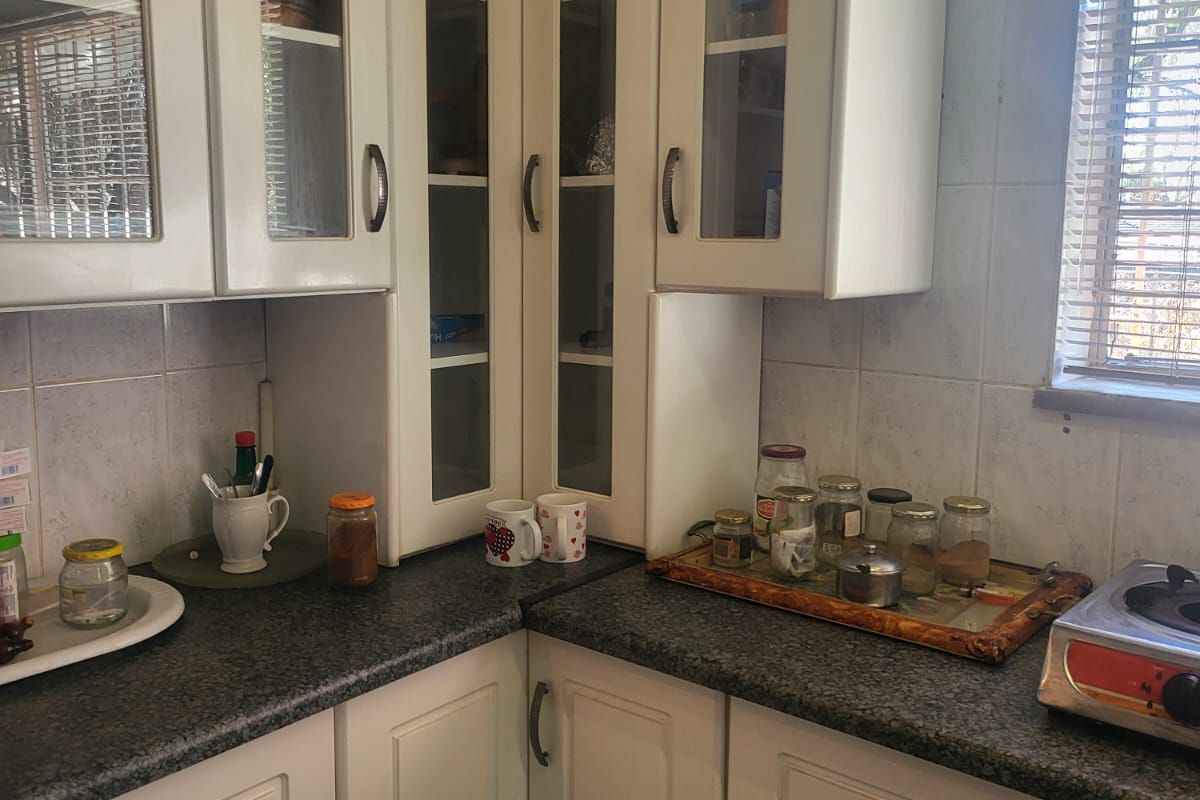 A functional kitchen corner featuring white built-in cabinetry with glass-fronted upper units, dark granite countertops, and a tiled backsplash.