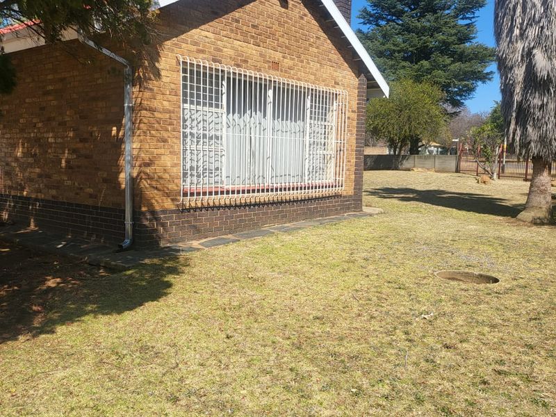 A view of the rear exterior of the face brick house, featuring security bars on the windows and a spacious garden area.