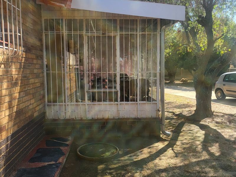 Front exterior view of a brick house featuring a covered porch area with security bars and paved walkway.
