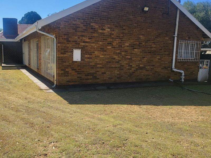 Rear view of the brick house featuring a tiled roof, security bars on windows, and a surrounding lawn area.