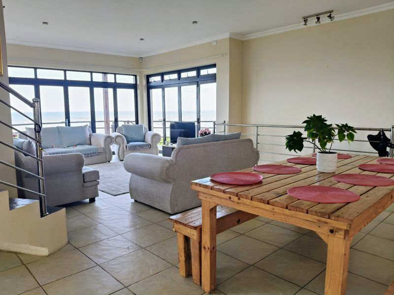 Spacious open-plan living and dining area featuring large glass doors with ocean views, tiled flooring, and modern stainless steel balustrades.