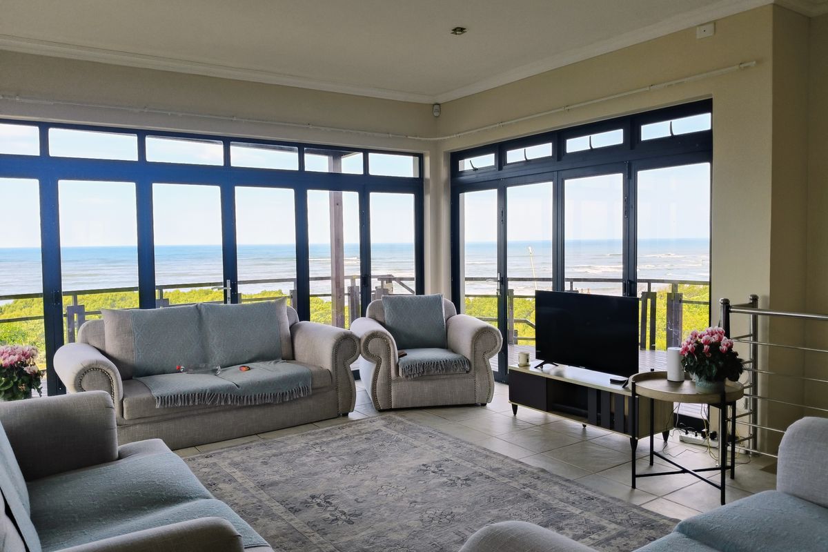 Spacious living room featuring expansive ocean views through large aluminium-framed windows, tiled flooring, and direct access to an outdoor balcony.