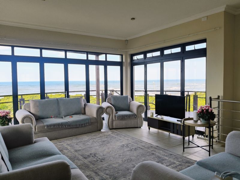 Spacious living room featuring expansive ocean views through large aluminium-framed windows, tiled flooring, and direct access to an outdoor balcony.