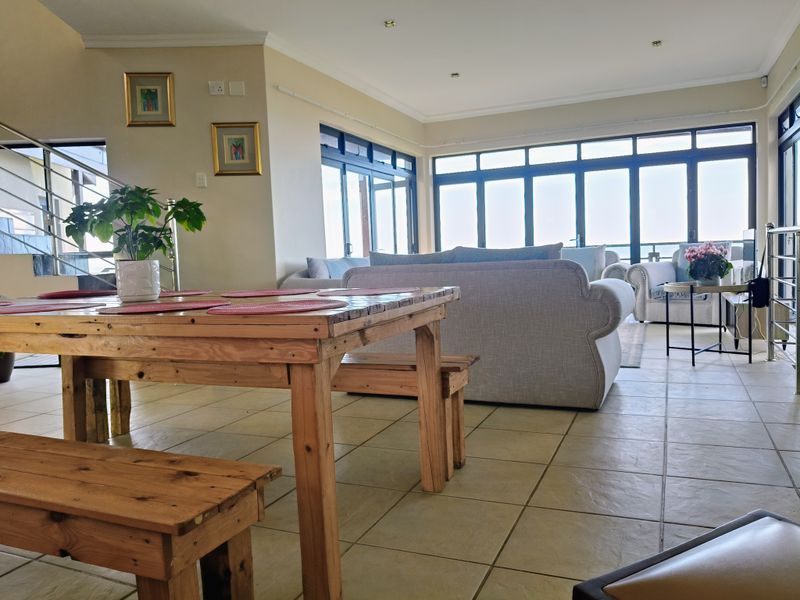 Spacious open-plan living and dining area featuring large aluminium-framed windows and sliding doors that provide ample natural light and access to the outdoors.