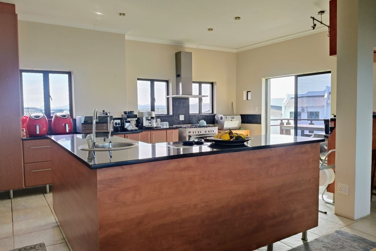 Spacious kitchen featuring a large central island with granite countertops, stainless steel appliances, and ample built-in cabinetry, opening onto an outdoor balcony area.