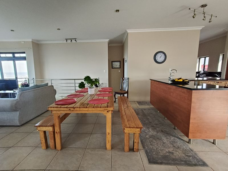 Open plan living and dining area featuring a kitchen island with granite countertops, tiled flooring, and access to a balcony with ocean views.
