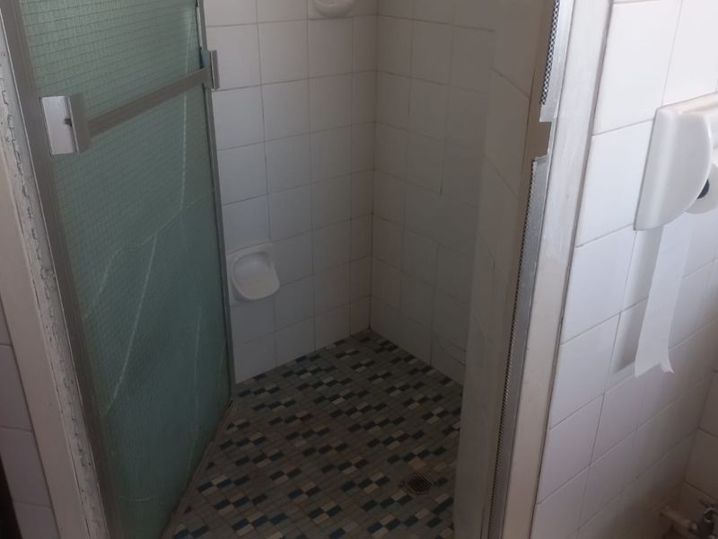 A compact bathroom featuring a shower enclosure with tiled walls and flooring, currently showing signs of wear and a cracked glass panel.