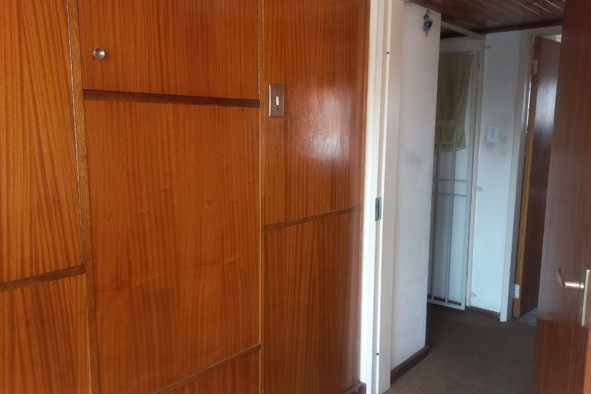 A hallway featuring built-in wooden cabinetry and timber ceiling details, leading to adjacent rooms with carpeted flooring.