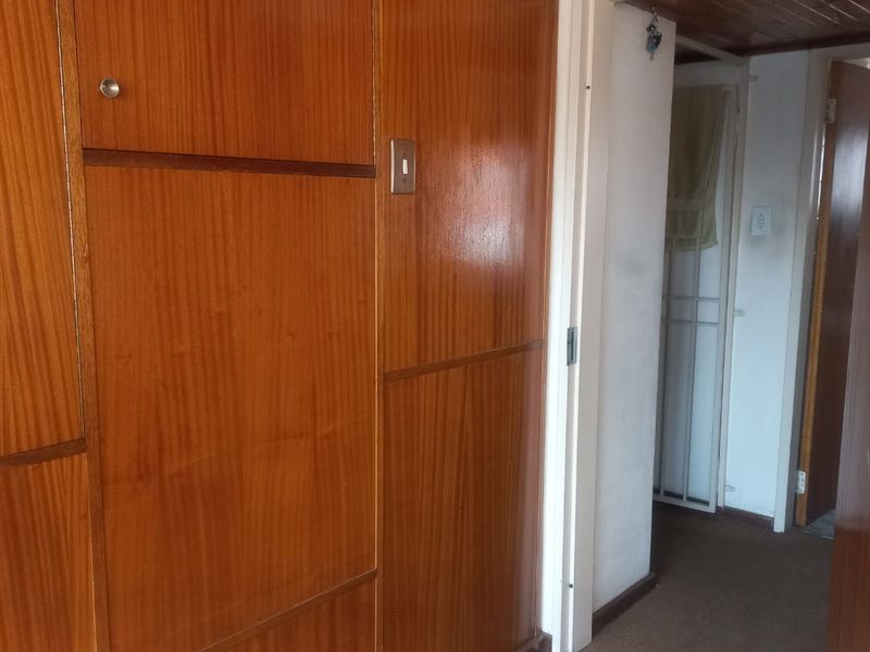 A hallway featuring built-in wooden cabinetry and timber ceiling details, leading to adjacent rooms with carpeted flooring.