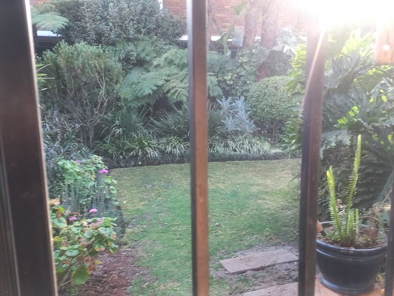 A view of a private garden area featuring established landscaping and a lawn, viewed through security bars from inside the property.