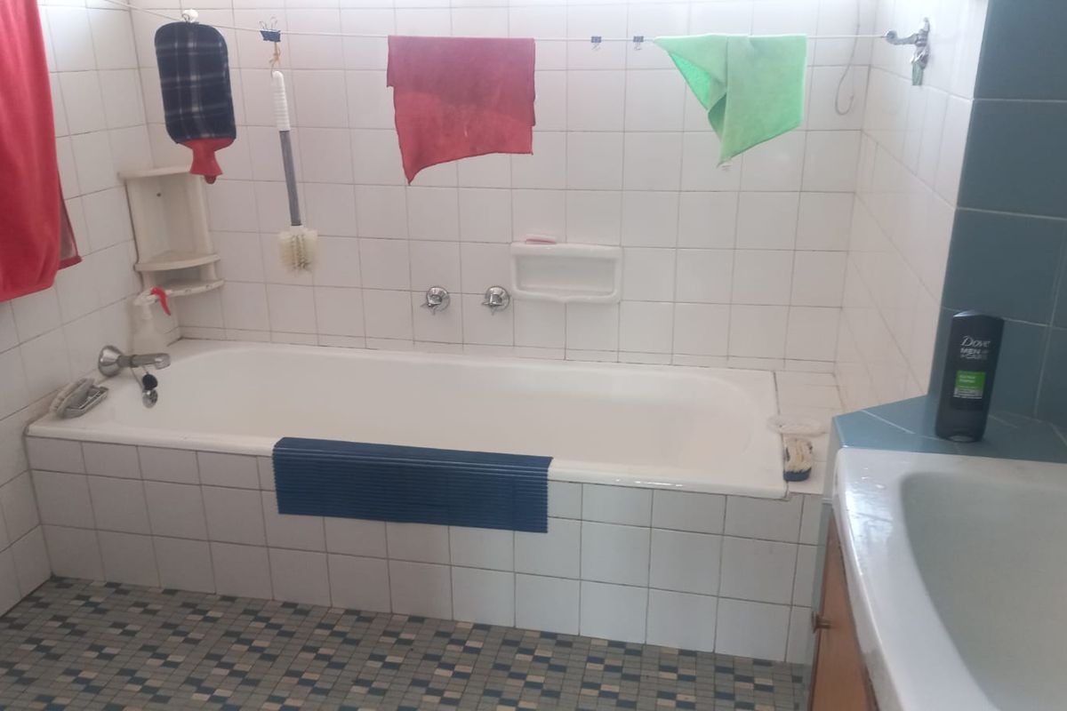 A dated bathroom featuring a built-in bathtub, tiled walls, and a vanity basin, requiring cosmetic updates to improve its overall aesthetic and appeal.