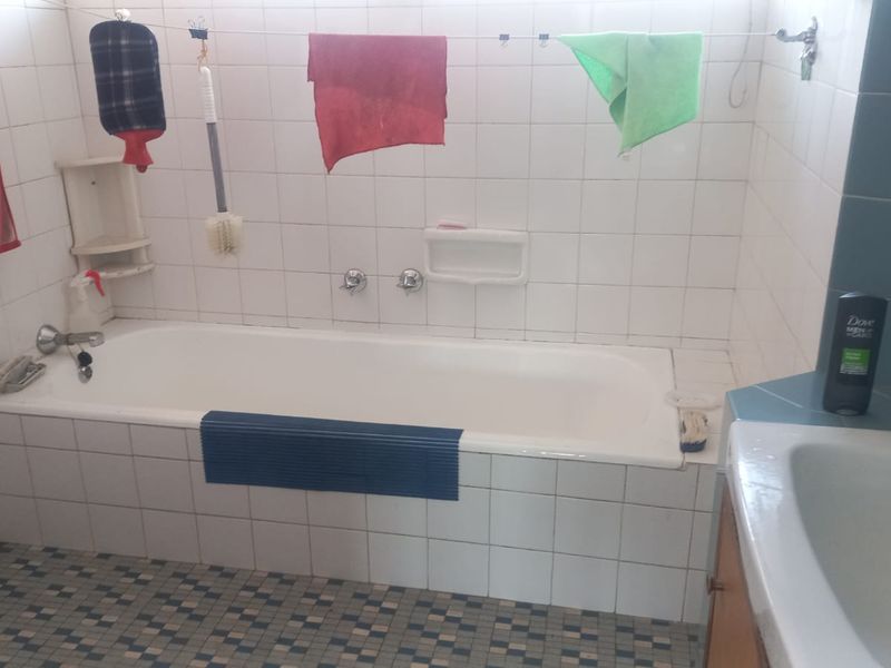 A dated bathroom featuring a built-in bathtub, tiled walls, and a vanity basin, requiring cosmetic updates to improve its overall aesthetic and appeal.