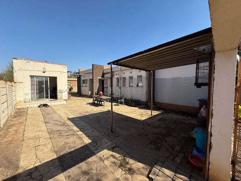 Rear exterior view featuring a paved courtyard, a covered patio area with metal roofing, and access to the main dwelling via a sliding door.