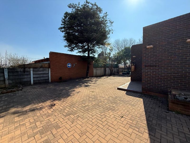 A paved rear courtyard area featuring face brick walls, perimeter fencing with razor wire, and established trees.