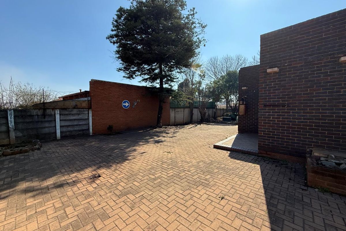 A paved rear courtyard area featuring face brick walls, perimeter fencing with razor wire, and established trees.