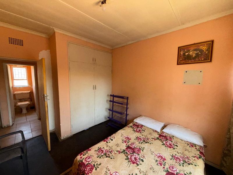 A bedroom featuring a built-in wardrobe and access to an en-suite bathroom, requiring cosmetic updates to the wall finishes.