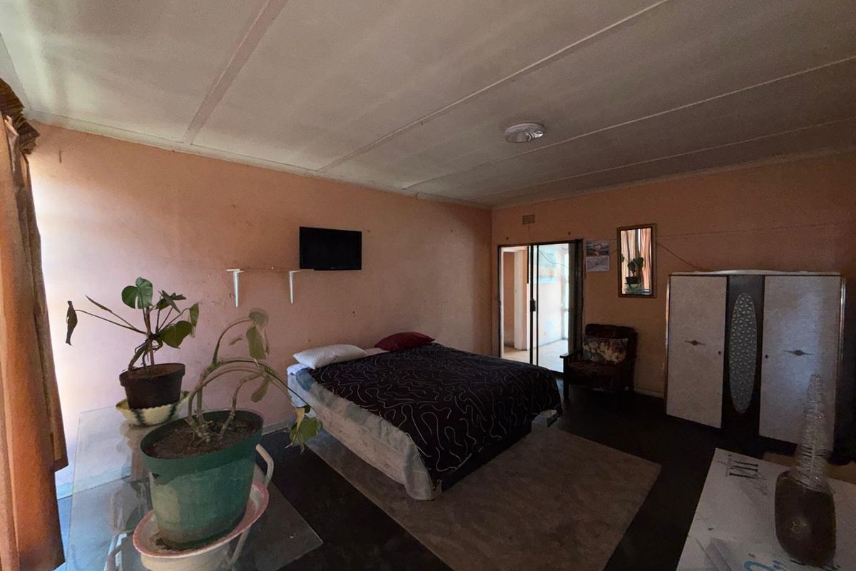 A bedroom featuring a sliding glass door leading to an outdoor area, with dated wall finishes and ceiling panels in need of maintenance.