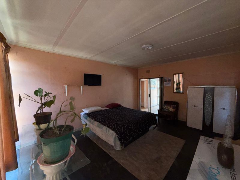 A bedroom featuring a sliding glass door leading to an outdoor area, with dated wall finishes and ceiling panels in need of maintenance.