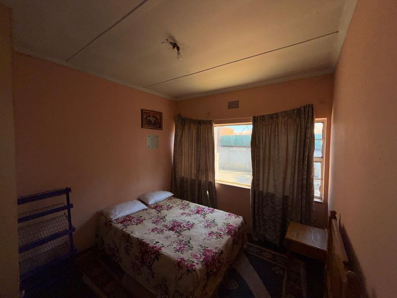 A bedroom featuring a window with curtains and a ventilation grille, showing signs of wear on the walls and ceiling.