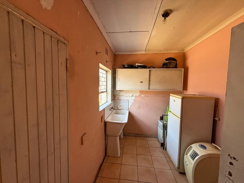 A functional laundry area featuring a ceramic utility sink, wall-mounted storage cabinetry, and tiled flooring, currently requiring cosmetic updates and wall repairs.