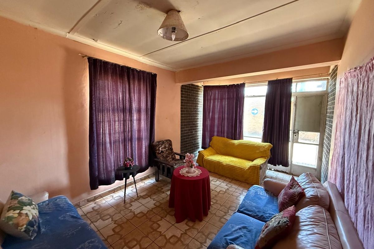 A living room featuring tiled flooring and an exposed brick wall, currently showing signs of ceiling water damage and requiring cosmetic updates.