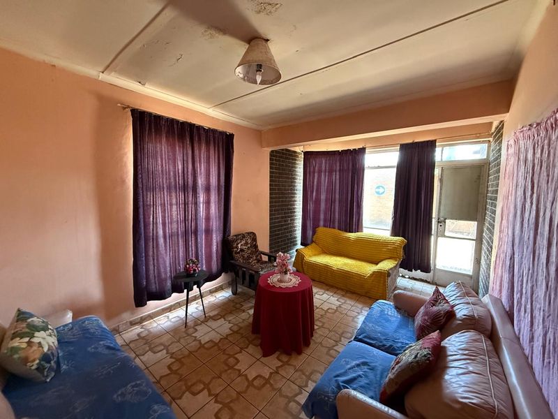 A living room featuring tiled flooring and an exposed brick wall, currently showing signs of ceiling water damage and requiring cosmetic updates.