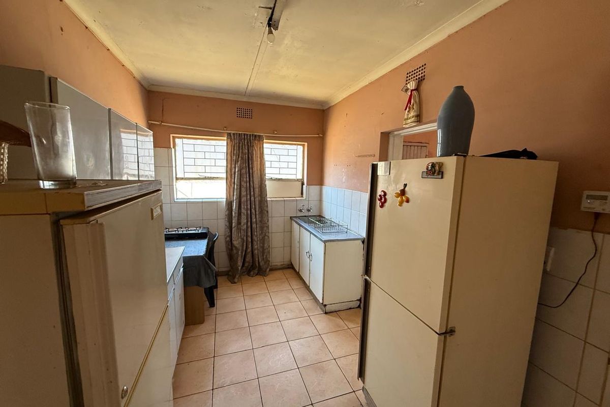 A dated kitchen featuring tiled flooring, basic cabinetry, and a tiled splashback, requiring cosmetic updates and repairs to the ceiling and wall finishes.