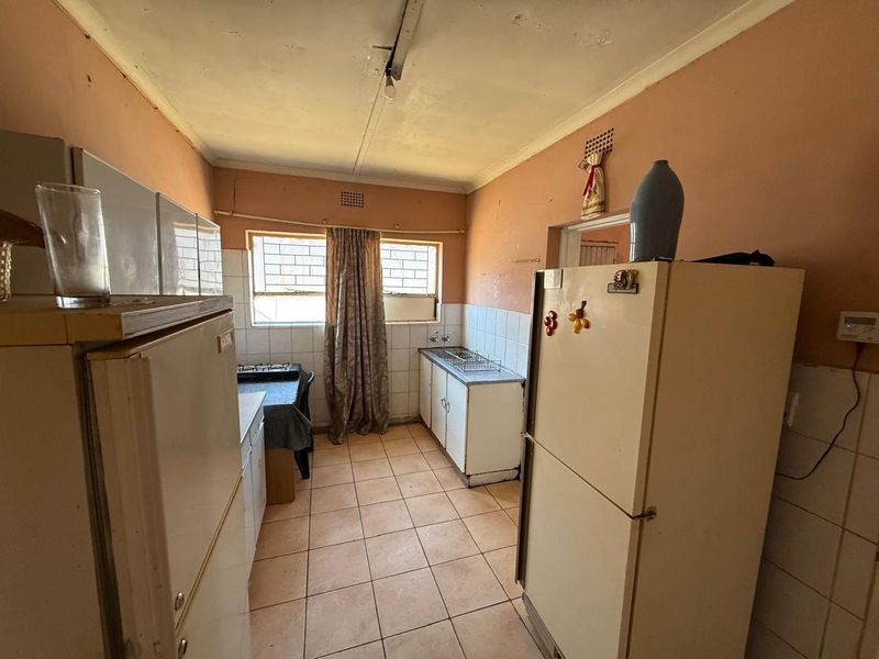 A dated kitchen featuring tiled flooring, basic cabinetry, and a tiled splashback, requiring cosmetic updates and repairs to the ceiling and wall finishes.