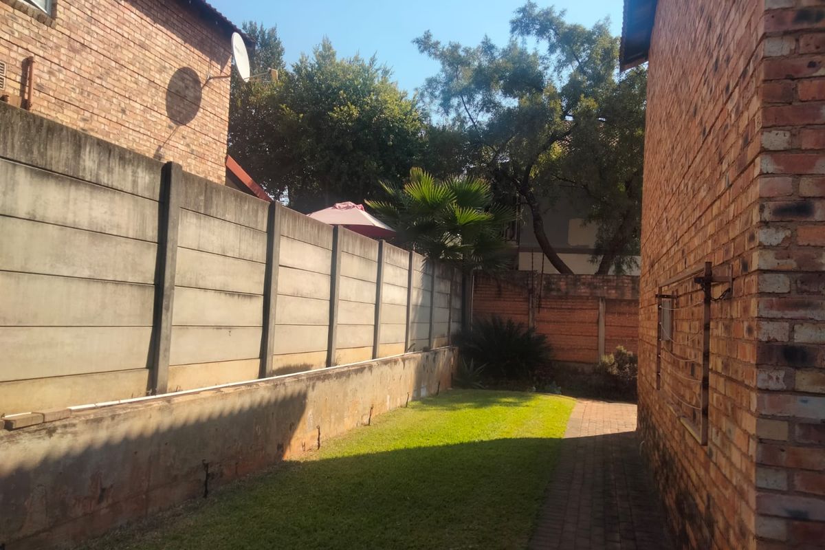 A side garden area featuring a brick-paved walkway, a small lawn, and a precast concrete boundary wall with a wall-mounted washing line.