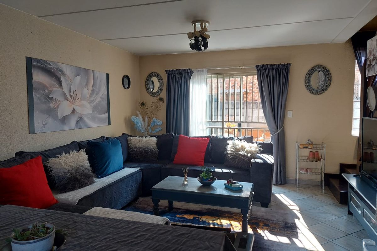 A comfortable living room featuring tiled flooring, a sliding door with security gate, and neutral wall finishes.