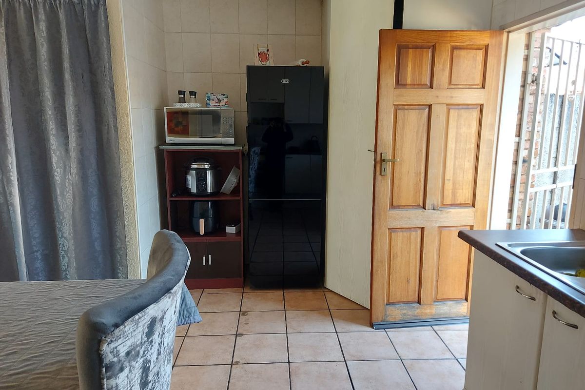 A functional kitchen area featuring tiled flooring, a timber door leading outdoors, and a compact sink area with laminate countertops.