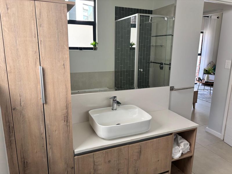 Modern bathroom featuring a vessel sink on a stone vanity, built-in cabinetry, and a glass-enclosed shower with stylish dark tiled accents.