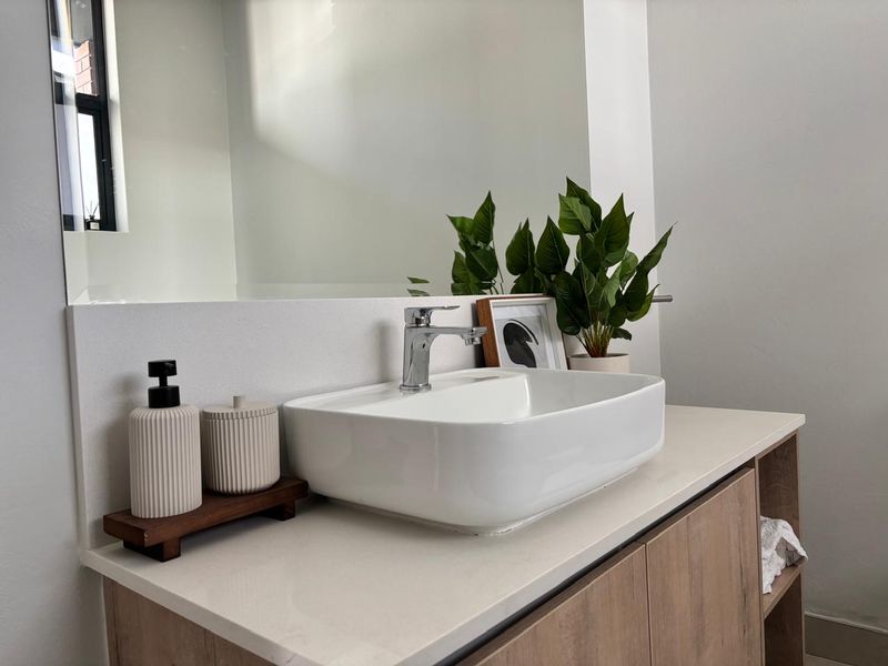 A modern bathroom vanity featuring a white vessel sink, chrome mixer tap, stone countertop, and a large wall-mounted mirror.